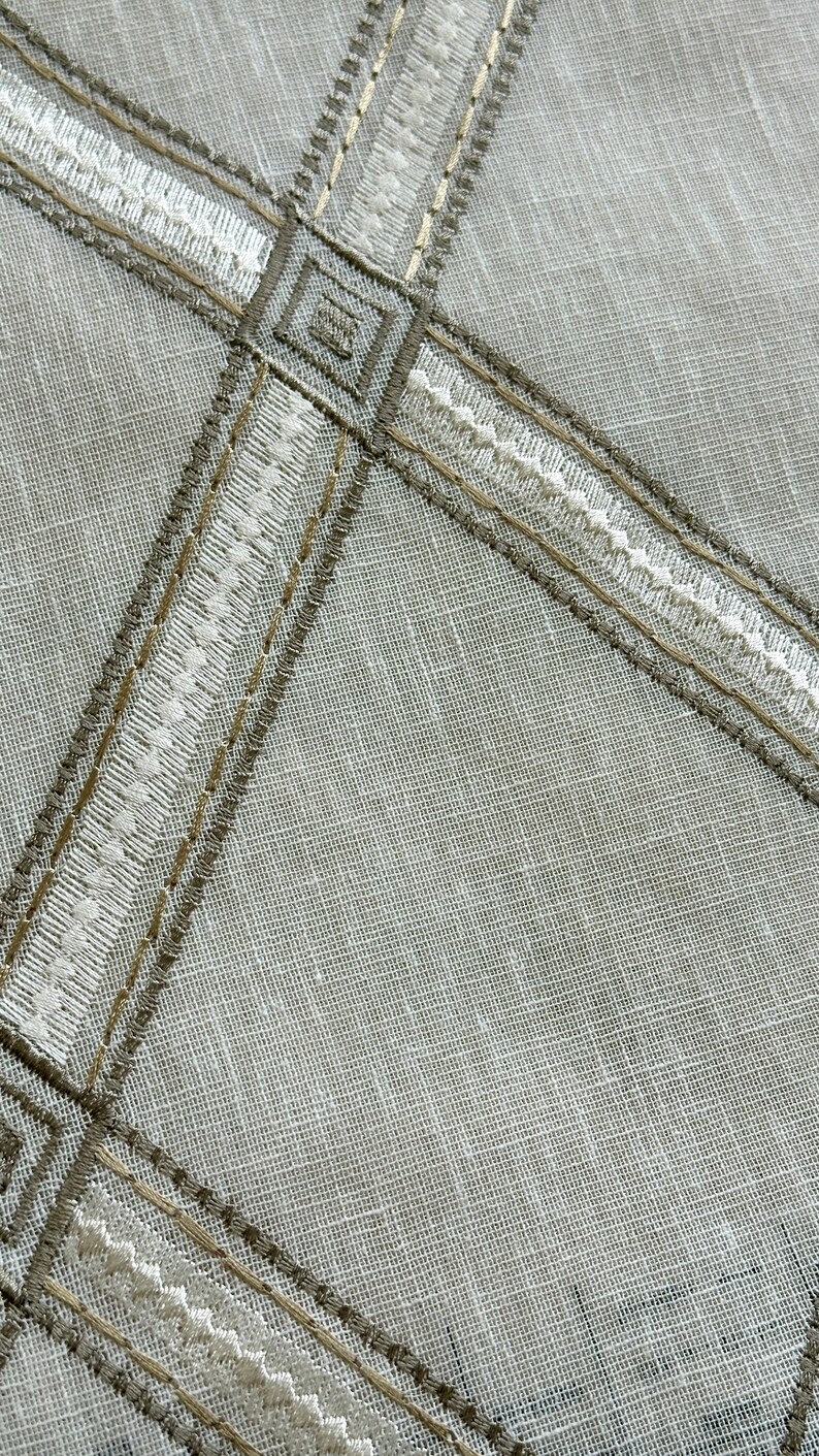 May include: A close-up of a white fabric with a brown and white embroidered design. The fabric has a subtle texture and a woven appearance.