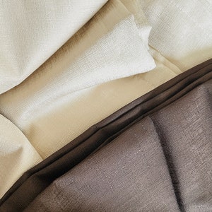 May include: Close-up of folded fabric in shades of cream and brown. The fabric has a textured appearance, with visible woven details. The folds create shadows and highlights, adding depth to the image. The overall aesthetic is simple and elegant.