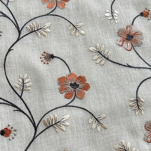 K&ouml;nnte beinhalten: Nahaufnahme eines beigefarbenen Stoffes mit gestickten Blumenmustern in Braun- und Oranget&ouml;nen. Der Stoff zeigt ein sich wiederholendes Muster aus zarten Blumen und Bl&auml;ttern.