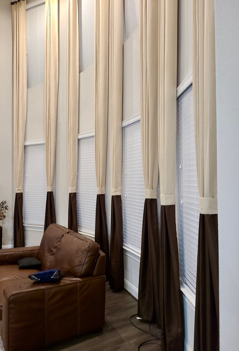 May include: Tall, elegant window curtains in a living room setting. The curtains are a combination of beige and dark brown, creating a two-tone effect. The beige fabric is at the top, transitioning to a dark brown at the bottom.