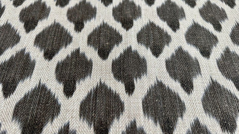May include: A close-up of a fabric with a white background and a black, abstract, ikat-style pattern.