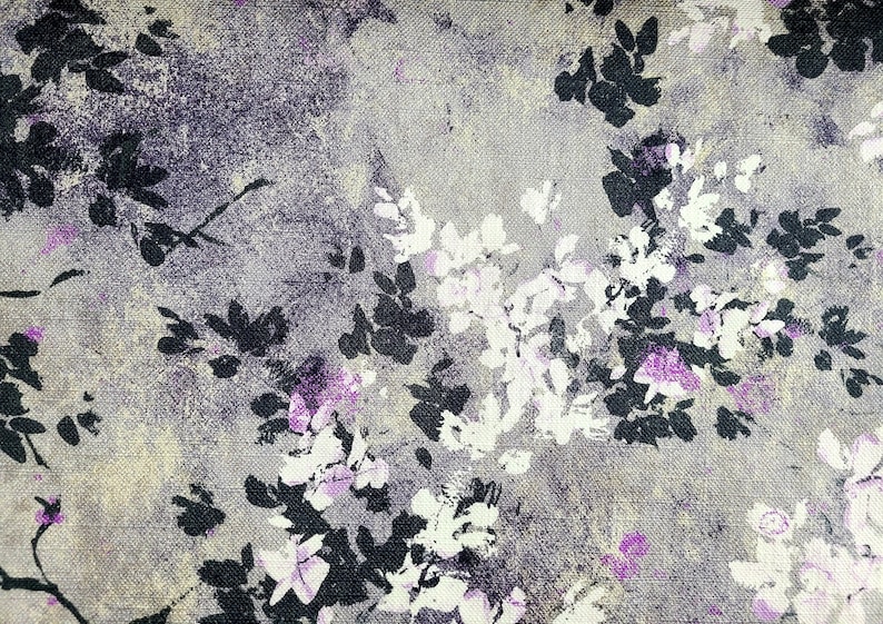 Pu&ograve; includere: Primo piano di un tessuto con un motivo floreale. Il tessuto &egrave; di colore grigio chiaro con una texture sottile. I fiori sono neri, bianchi e viola.