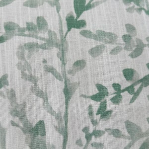 May include: A white fabric with a green leafy pattern. The fabric has a subtle texture.