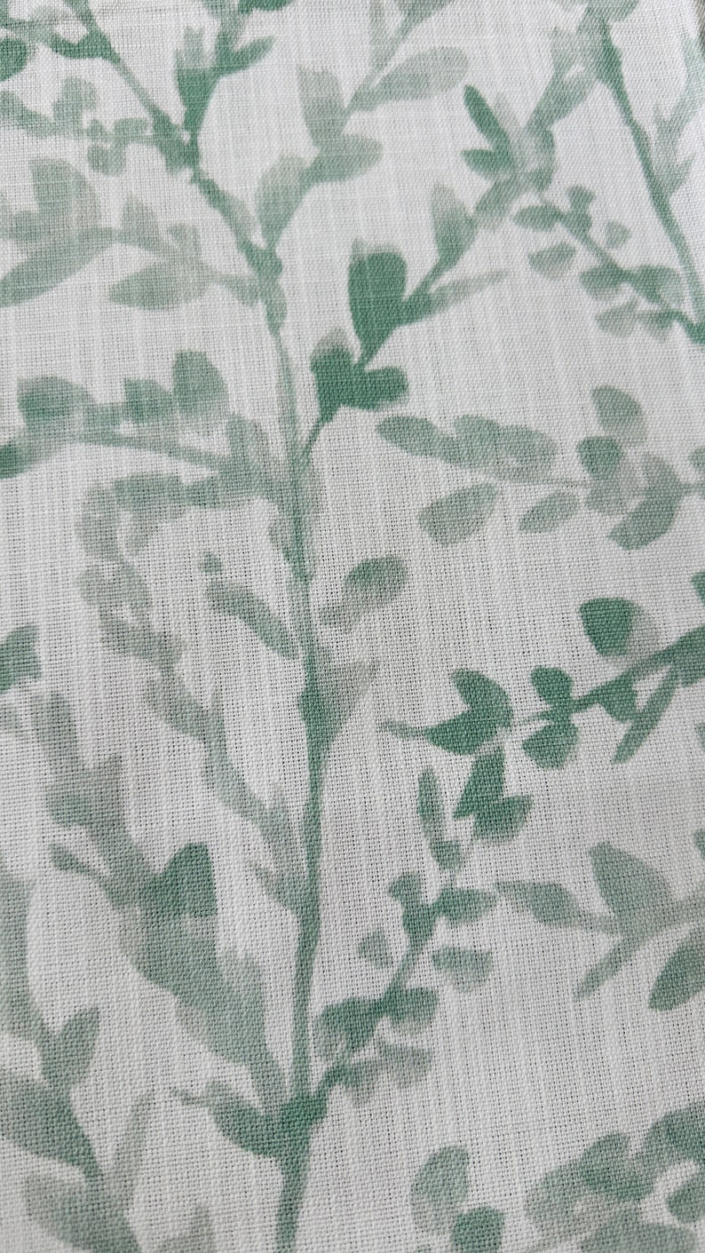 May include: A white fabric with a green leafy pattern. The fabric has a subtle texture.