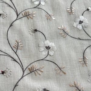 May include: White embroidered flowers on a beige linen fabric. The flowers are delicate and have a simple design. The fabric is soft and has a subtle texture.