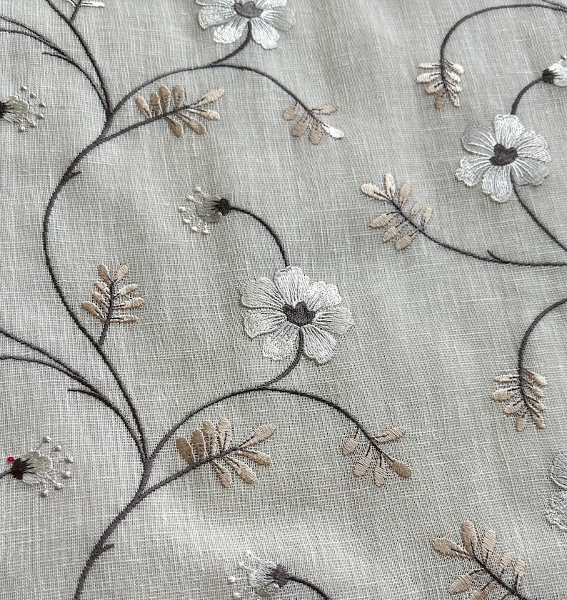 May include: White embroidered flowers on a beige linen fabric. The flowers are delicate and have a simple design. The fabric is soft and has a subtle texture.