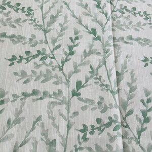 May include: A white fabric with a green leafy pattern. The leaves are a watercolor style and are scattered across the fabric.