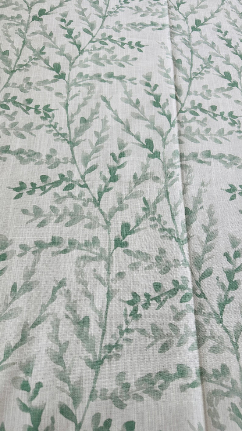 May include: A white fabric with a green leafy pattern. The leaves are a watercolor style and are scattered across the fabric.