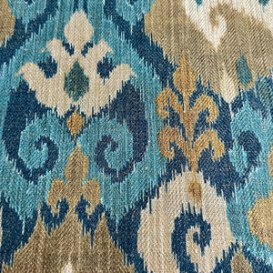 May include: Blue, beige, and gold patterned fabric with an ikat design. The fabric has a woven texture.