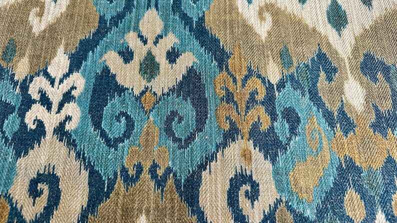 May include: Blue, beige, and gold patterned fabric with an ikat design. The fabric has a woven texture.