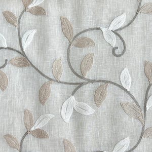 May include: A close-up of a beige fabric with an embroidered design of brown and white leaves and vines.