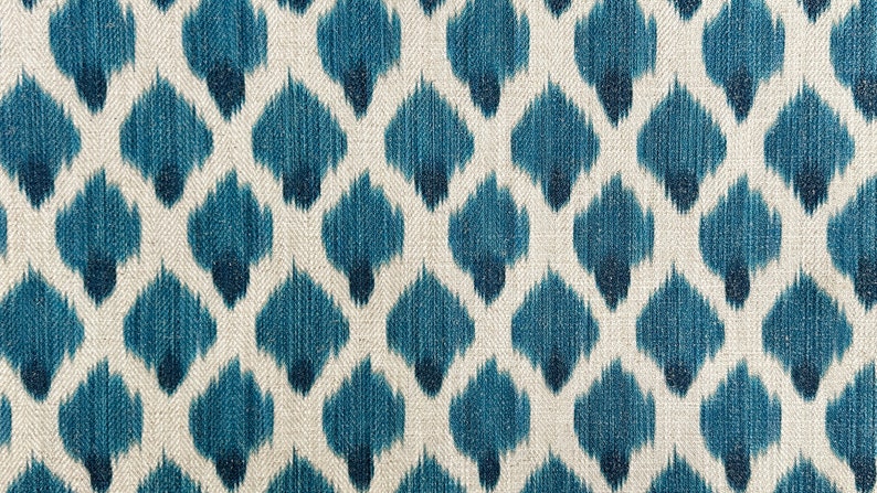May include: A close-up of a fabric with a repeating pattern of blue and white ikat-style shapes. The fabric has a textured, woven look.