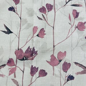 May include: A white fabric with a repeating pattern of purple watercolor flowers and stems. The flowers are stylized and resemble a simple blossom.