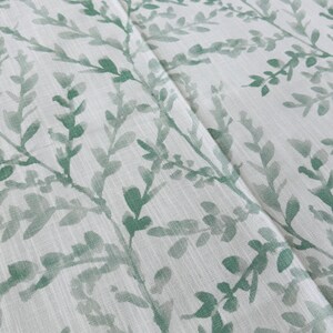 May include: A white fabric with a green leafy pattern. The leaves are a watercolor style and are scattered across the fabric.