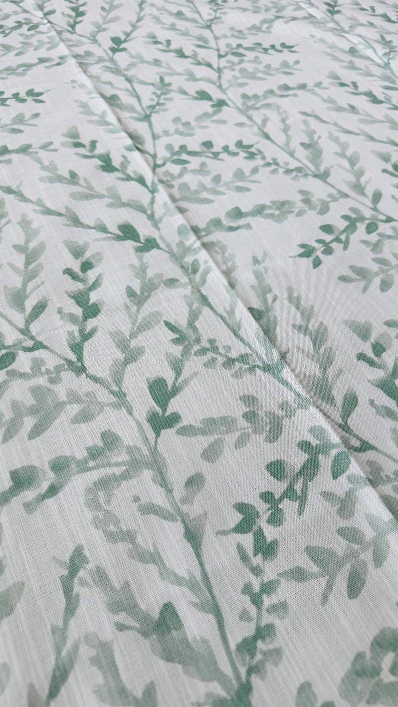 May include: A white fabric with a green leafy pattern. The leaves are a watercolor style and are scattered across the fabric.
