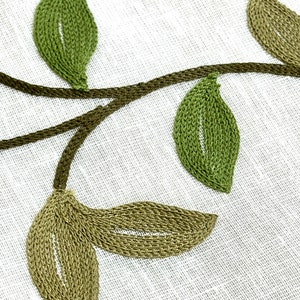 May include: Embroidered green leaves and vines on a white linen fabric background.