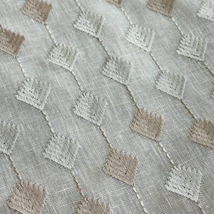 Puede incluir: Tela blanca con un patr&oacute;n geom&eacute;trico de rombos bordados en marr&oacute;n y blanco.