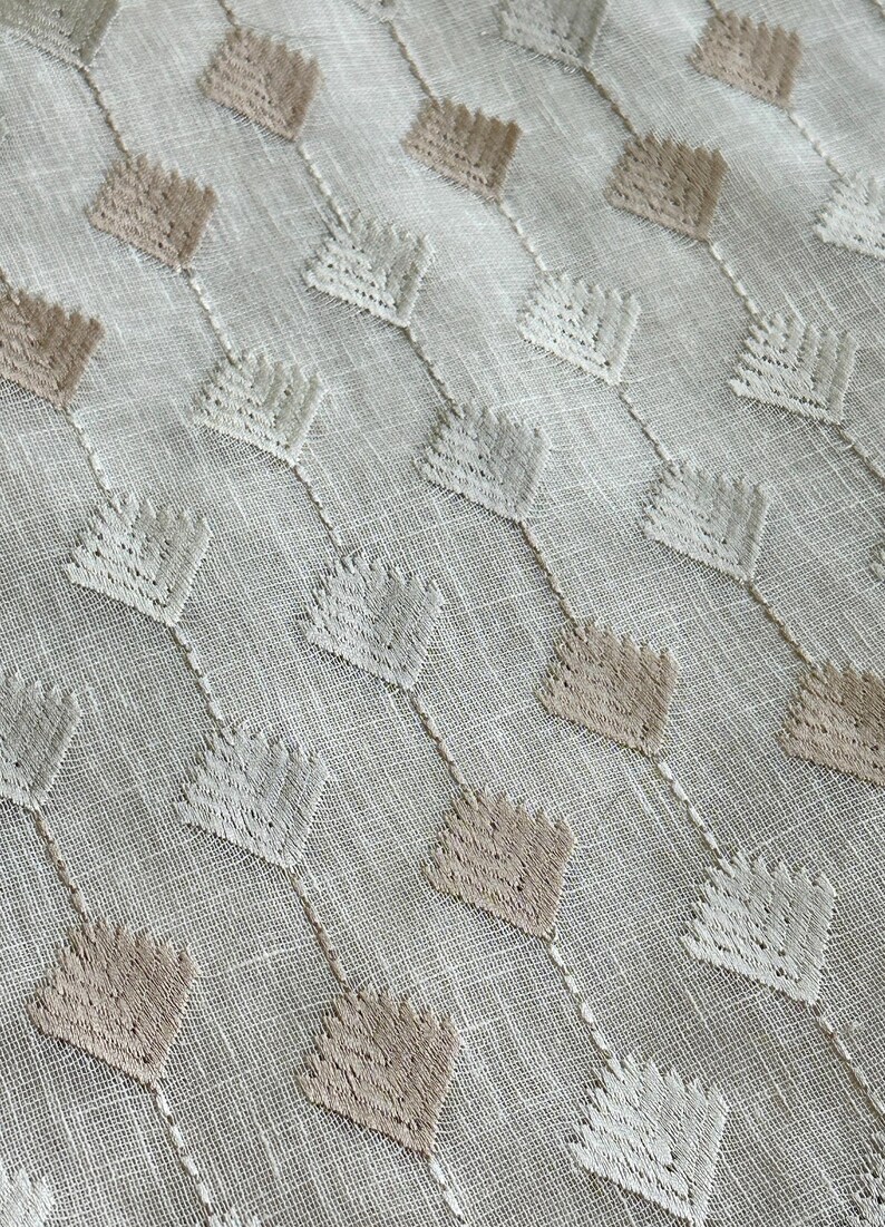 Puede incluir: Tela blanca con un patr&oacute;n geom&eacute;trico de rombos bordados en marr&oacute;n y blanco.