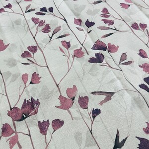 May include: A white fabric with a repeating pattern of delicate, watercolor-style pink and purple flowers and stems.