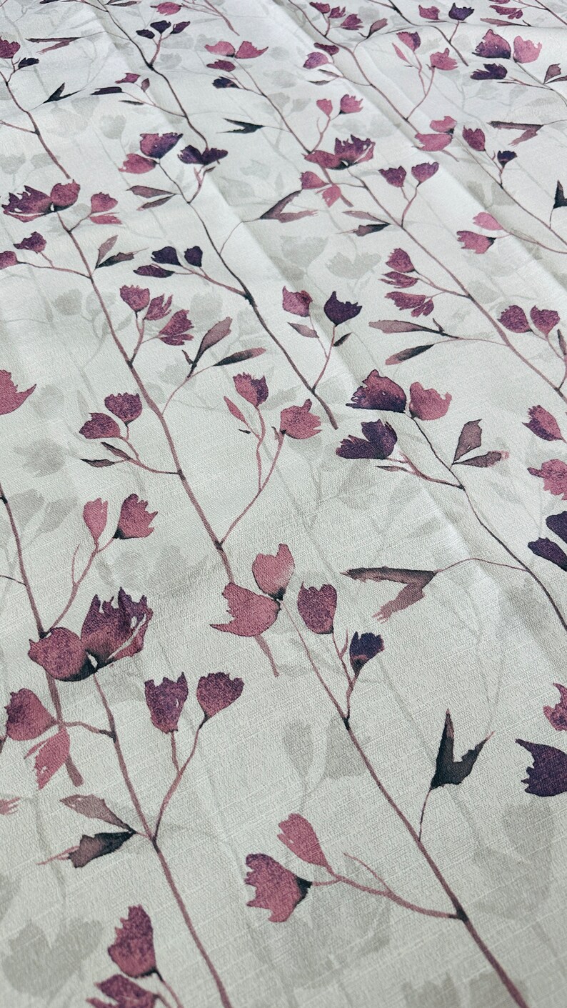 May include: A white fabric with a repeating pattern of delicate, watercolor-style pink and purple flowers and stems.