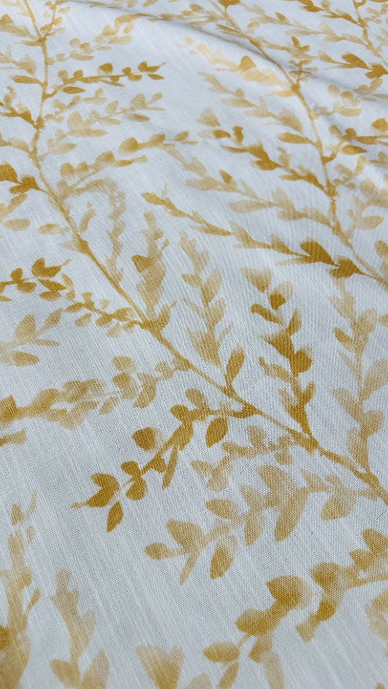 May include: White fabric with a subtle pattern of gold-colored leaves and branches.