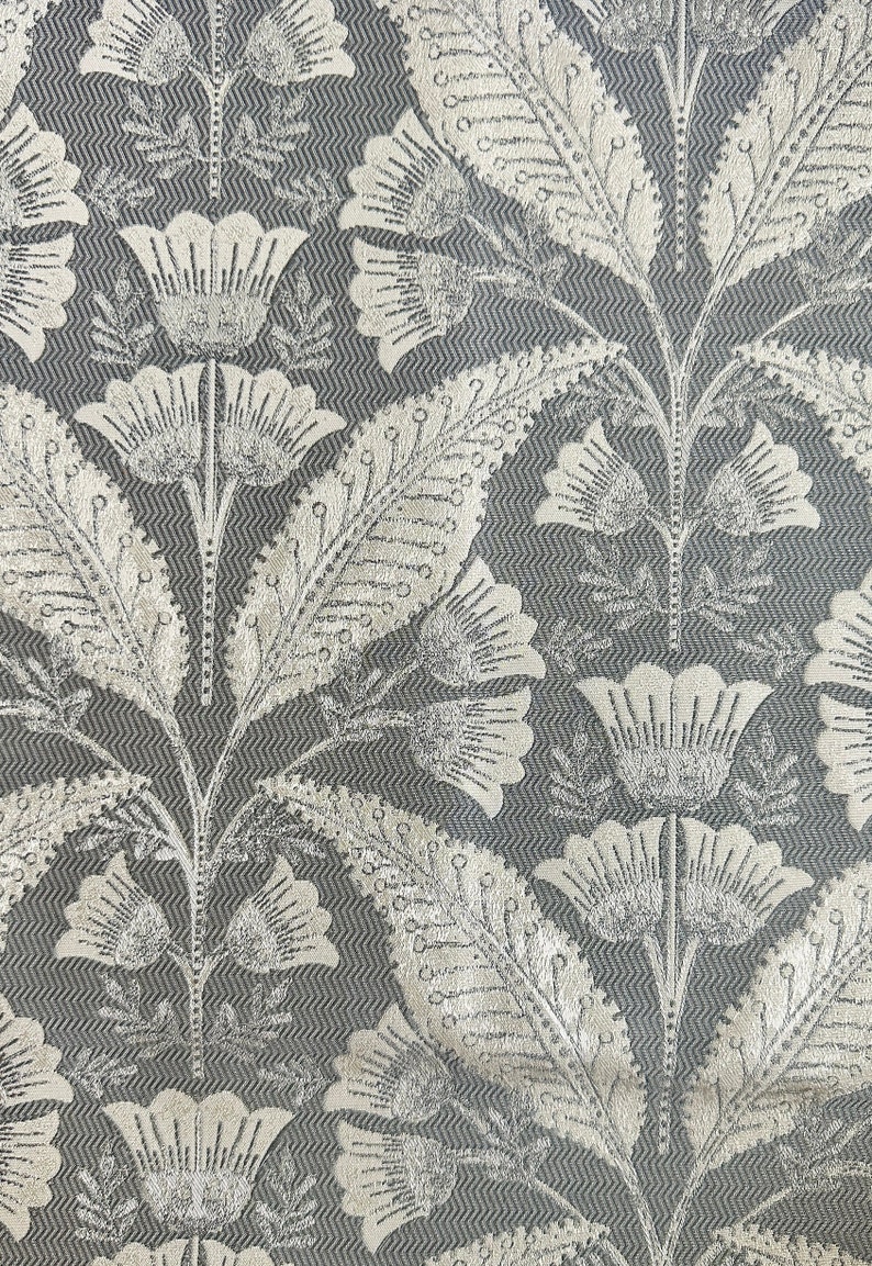Pu&ograve; includere: Primo piano di un tessuto grigio con un motivo floreale argentato. Il motivo presenta fiori e foglie stilizzati.