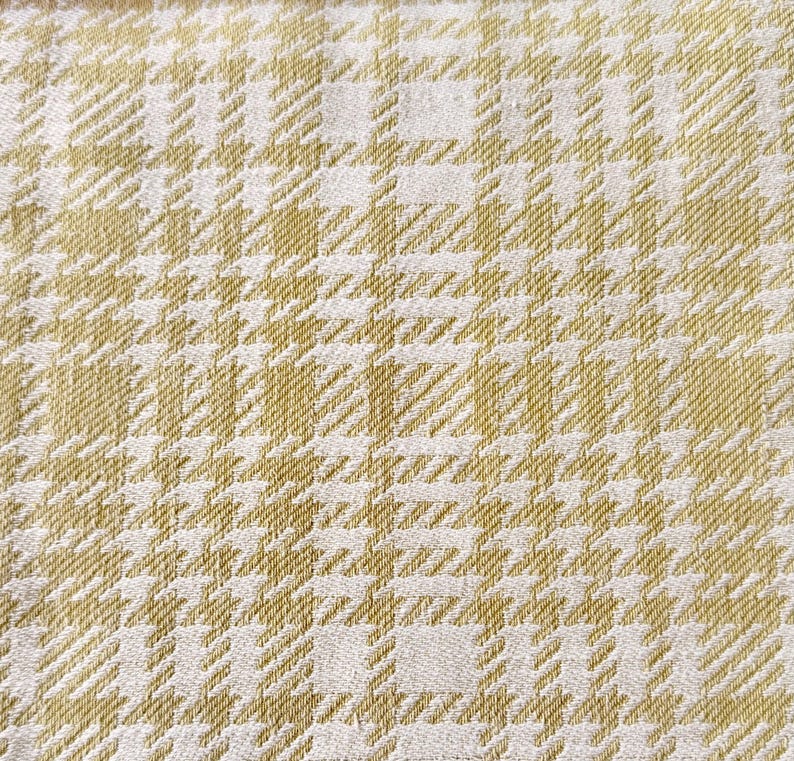May include: A woven fabric featuring a repeating houndstooth pattern in shades of light olive green and off-white. The textile displays a dense, textured weave with a consistent grid-like structure throughout the entire surface area.