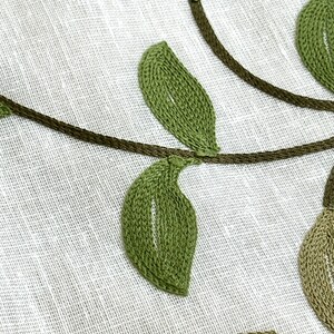 May include: Close-up of a white fabric with green embroidered leaves and vines. The leaves are stitched with a detailed, textured pattern.