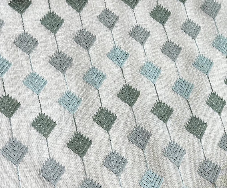 May include: A white fabric with a repeating pattern of blue and green diamond shapes. The diamonds are made of a textured, embroidered design.