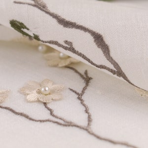 May include: White fabric with embroidered brown branches and beige flowers with pearl centers.