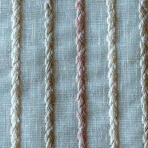 Puede incluir: Primer plano de una tela tejida con rayas alternas de color beige y rosa claro.