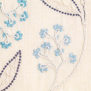 Puede incluir: Primer plano de una tela color crema con patrones florales y de hojas bordados. El bordado presenta hilo azul claro y azul oscuro, con contornos de cord&oacute;n blanco. El dise&ntilde;o incluye flores y hojas estilizadas.