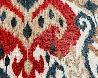 May include: Close-up of a fabric with a red, brown, and blue ikat pattern. The fabric has a woven texture and a repeating design.