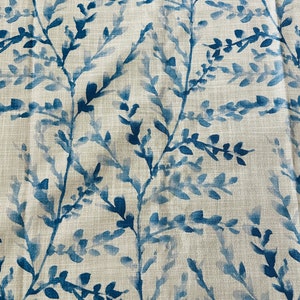 May include: Close-up of fabric with a repeating pattern of blue watercolor-style branches and leaves against a neutral beige background. The design has a natural, botanical theme, suitable for home decor.