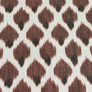 May include: A white fabric with a brown and black ikat pattern. The pattern is a repeating design of small, diamond-shaped figures.