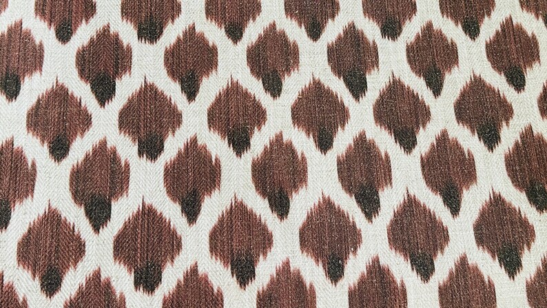 May include: A white fabric with a brown and black ikat pattern. The pattern is a repeating design of small, diamond-shaped figures.