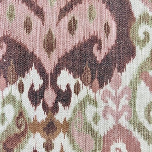 May include: Close-up of a woven fabric with an ikat pattern. The design features repeating abstract shapes in shades of brown, pink, green, and off-white. The texture of the fabric is visible, adding depth to the design.