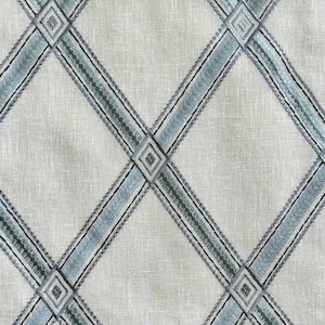 May include: A close-up of a fabric with a criss-cross pattern. The fabric is a light beige color with blue and green stripes.
