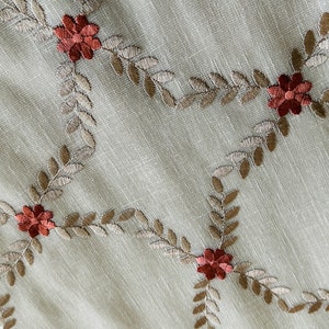 Puede incluir: Tela beige con un patr&oacute;n repetido de hojas marrones y flores rojas bordadas.