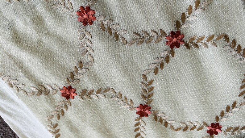 Puede incluir: Tela beige con un patr&oacute;n repetido de hojas marrones y flores rojas bordadas.
