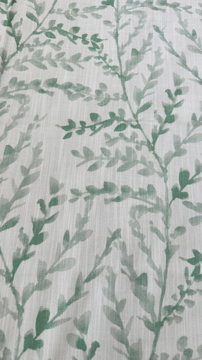 May include: A white fabric with a green leafy pattern. The leaves are a watercolor style and are scattered across the fabric.