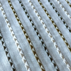 May include: White fabric with diagonal stripes of white, brown, and gray thread.