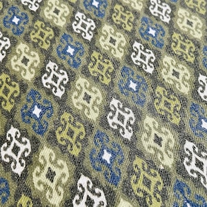May include: A close-up of a fabric with a repeating pattern of blue, white, and green geometric shapes. The fabric has a textured surface.
