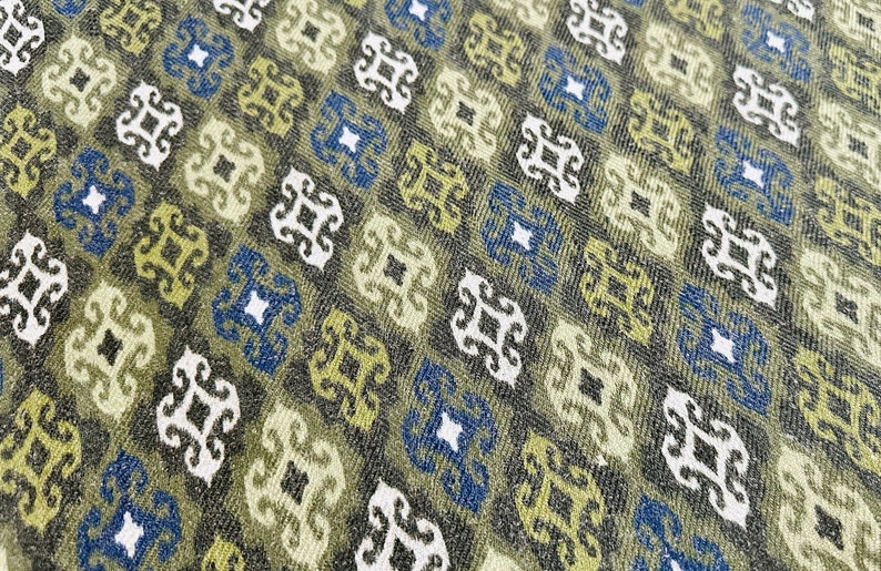 May include: A close-up of a fabric with a repeating pattern of blue, white, and green geometric shapes. The fabric has a textured surface.