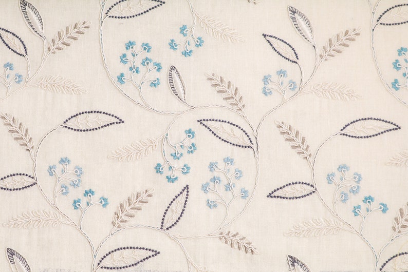 Puede incluir: Tela color crema con un patr&oacute;n floral bordado. El dise&ntilde;o presenta delicadas flores azules, hojas de color gris-marr&oacute;n y tallos punteados azul oscuro. El bordado crea un aspecto texturizado y elegante, adecuado para la decoraci&oacute;n del hogar.