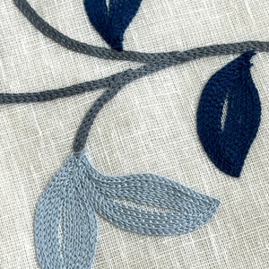 May include: Close-up of embroidered fabric with a blue and gray floral design. The fabric has a woven texture and the embroidery is detailed.
