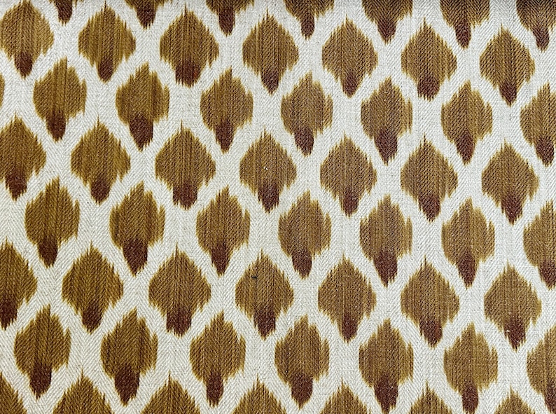May include: A white fabric with a brown and red ikat pattern. The pattern is a repeating design of small, teardrop-shaped figures.