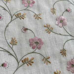 Puede incluir: Primer plano de una tela blanca con flores rosas y hojas doradas bordadas. La tela tiene una textura sutil.