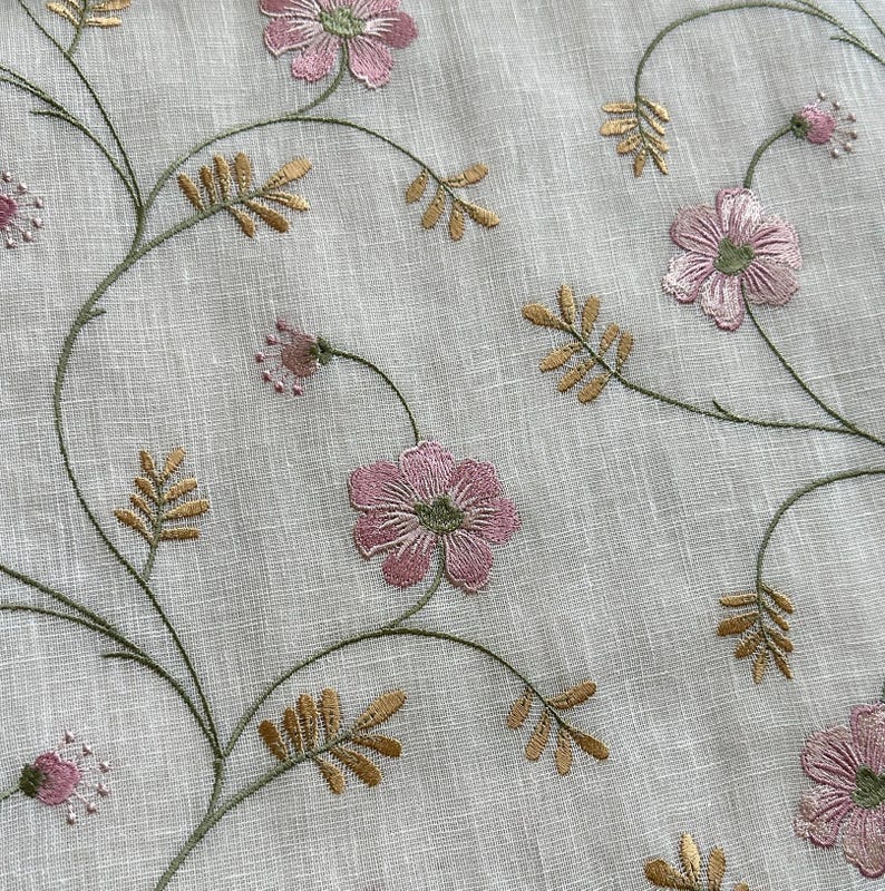 Puede incluir: Primer plano de una tela blanca con flores rosas y hojas doradas bordadas. La tela tiene una textura sutil.