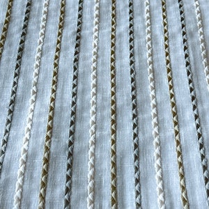 May include: White fabric with vertical stripes of white, gray, and brown thread. The stripes are woven into the fabric and have a textured appearance.